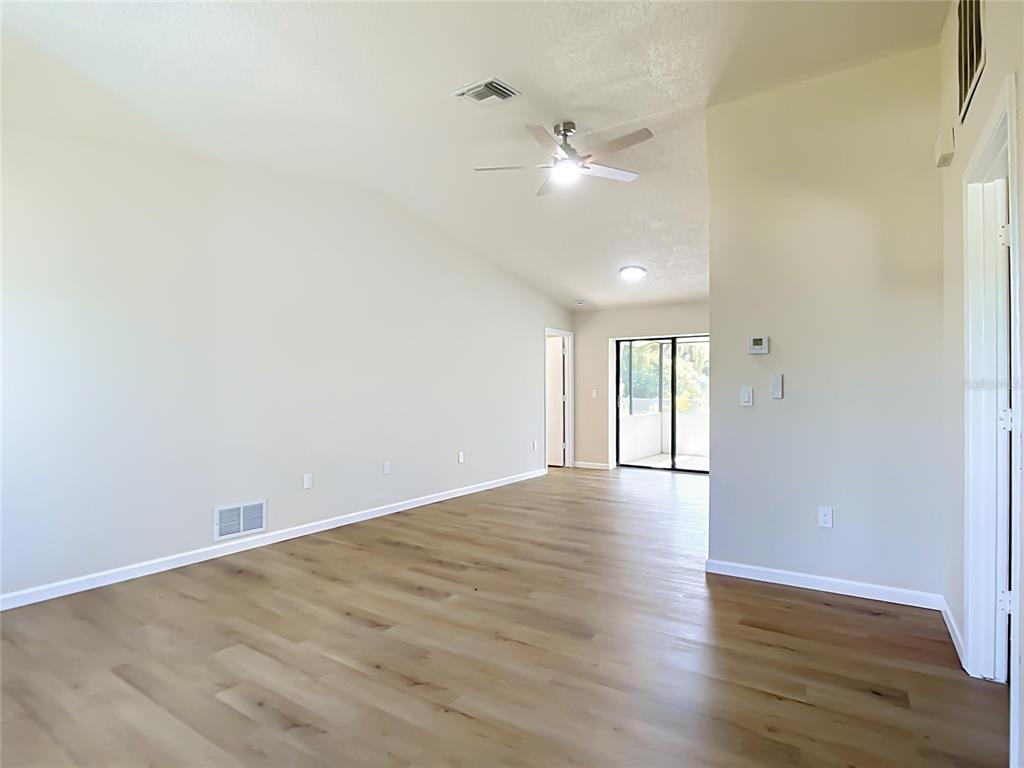 An empty living room with light wood-look flooring, a ceiling fan, and a sliding glass door — 4441 MULGRAVE AVENUE, NORTH PORT, FL