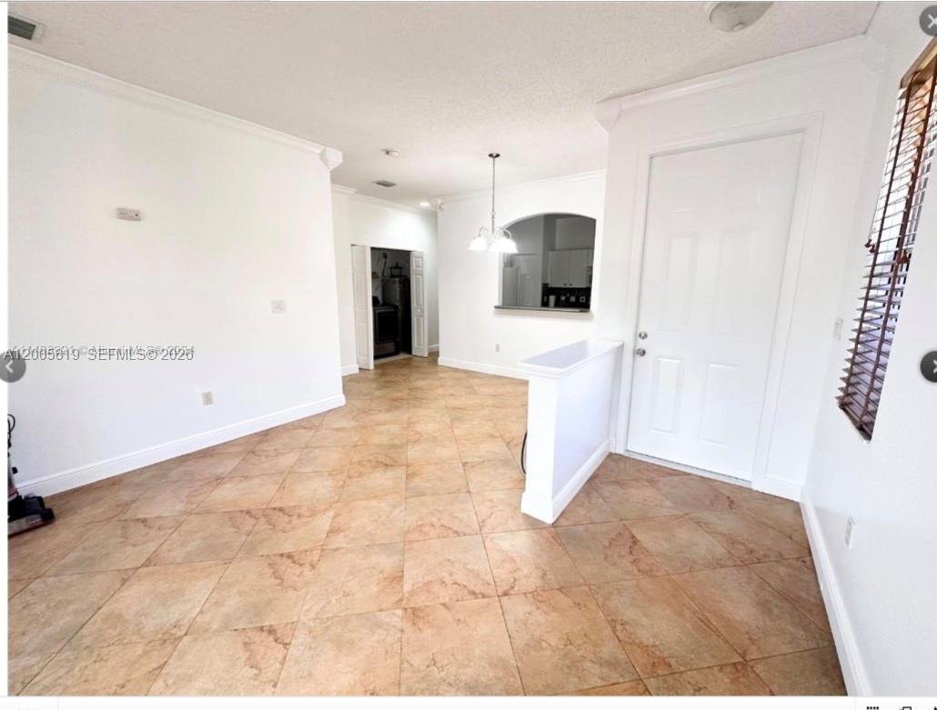 An interior view of a room with tan tile flooring, white walls, and a pass-through window — 4268 NE 9th St, Homestead FL 33033, HOMESTEAD, FL