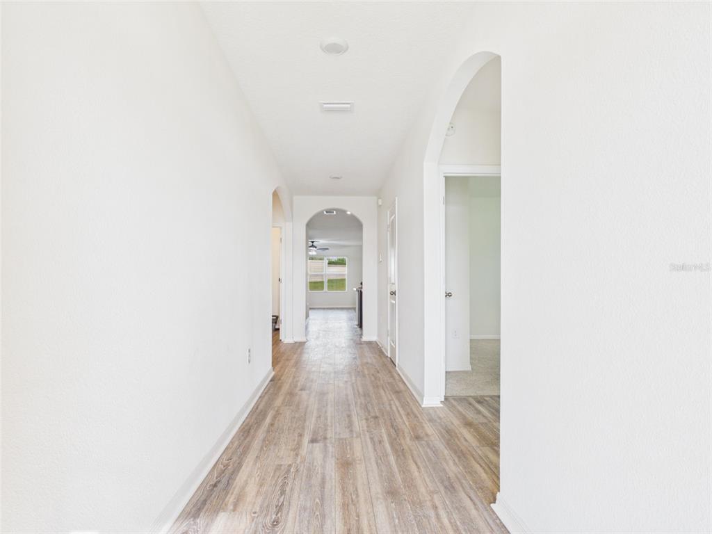 A hallway with light wood-look flooring leads to an arched doorway and a distant window — 4942 SW 97TH LANE, OCALA, FL