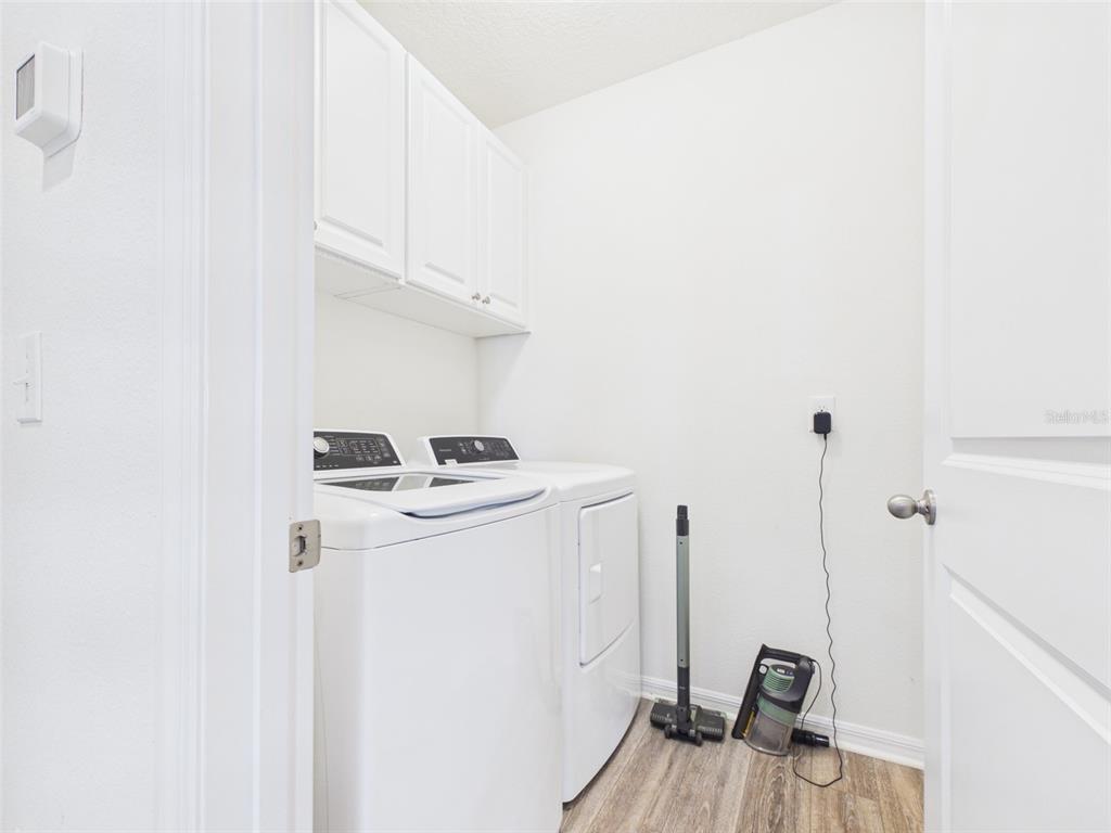 A laundry room features white appliances, upper cabinets, and wood-look flooring — 4942 SW 97TH LANE, OCALA, FL