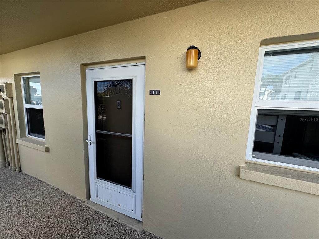 A beige exterior wall features a white storm door labeled 111 and two windows — 1400 TARPON CENTER DRIVE UNIT 111, VENICE, FL