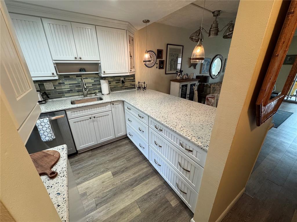 A kitchen features white beadboard cabinets, speckled countertops, a tile backsplash, and wood-look flooring — 1400 TARPON CENTER DRIVE UNIT 111, VENICE, FL