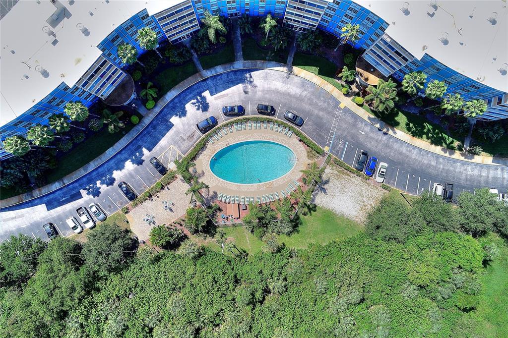 An aerial view shows a curved apartment building surrounding a swimming pool and parking lot — 3315 58TH AVENUE S UNIT 513, ST PETERSBURG, FL