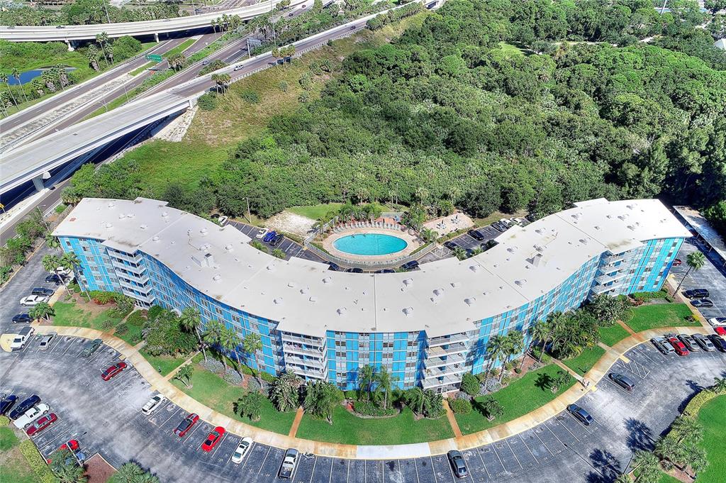 An aerial view shows a curved apartment building with a central pool and parking lots — 3315 58TH AVENUE S UNIT 513, ST PETERSBURG, FL