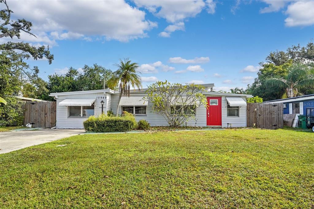 A single-story house with light-colored siding, a bright red front door, and a grassy yard — 10949 105TH STREET, LARGO, FL