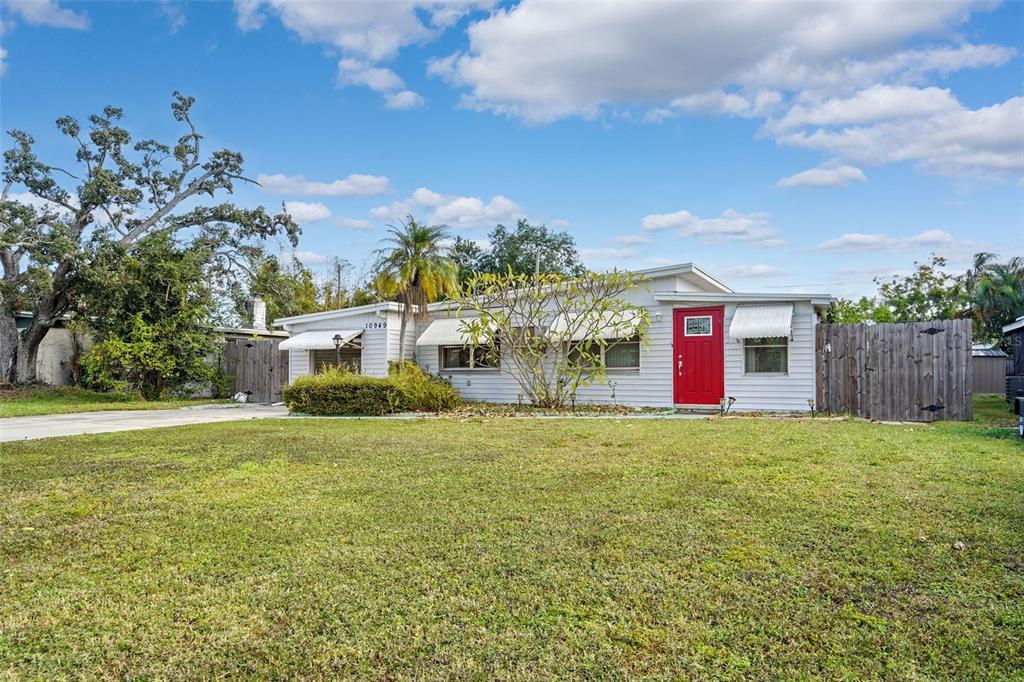 A single-story house with white horizontal siding, a bright red front door, and a lawn — 10949 105TH STREET, LARGO, FL