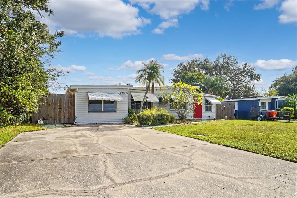 A single-story house with light siding, a red front door, and a cracked concrete driveway — 10949 105TH STREET, LARGO, FL