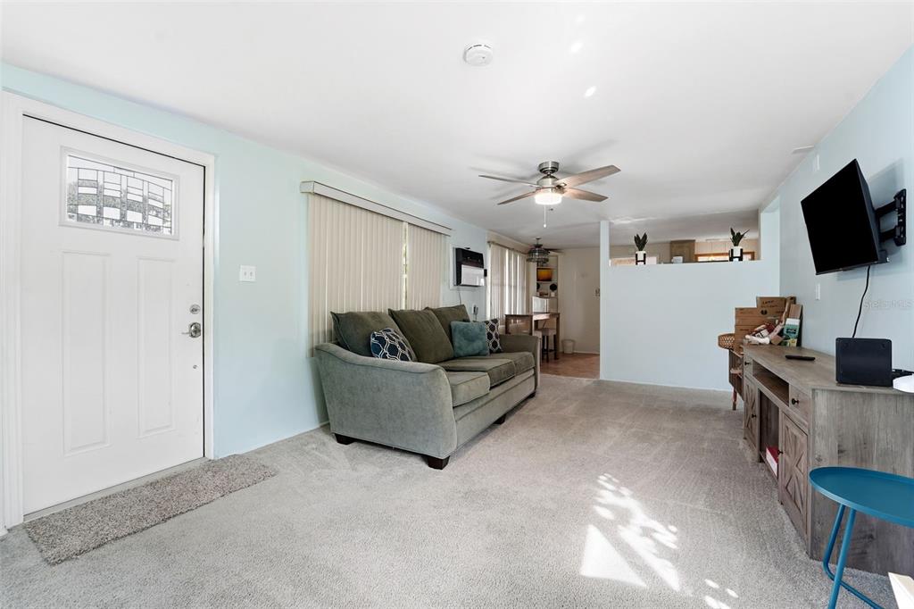 A living room with light blue walls, gray carpet, a sofa, and a wall-mounted television — 10949 105TH STREET, LARGO, FL