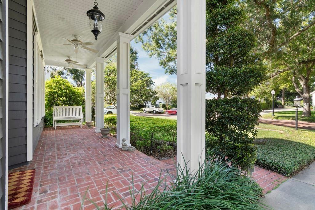 A covered brick porch features white columns, a bench, and ceiling fans overlooking a yard — 1119 BELLEAIRE CIRCLE, ORLANDO, FL