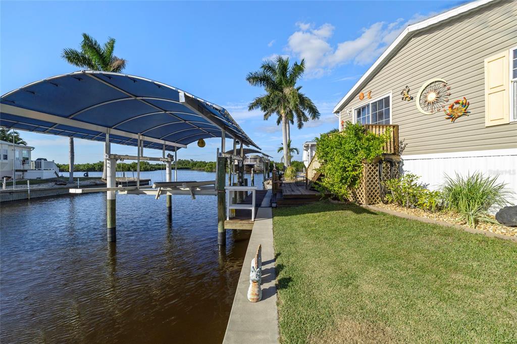 A waterfront home features a boat lift, a grassy yard, and a wooden deck — 3413 BAYSIDE PARKWAY, PUNTA GORDA, FL