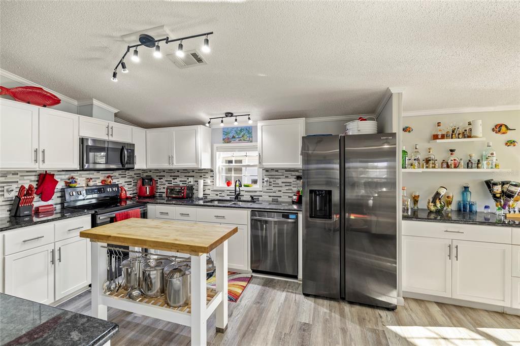 A kitchen with white cabinets, stainless steel appliances, a wooden island, and a tile backsplash — 3413 BAYSIDE PARKWAY, PUNTA GORDA, FL