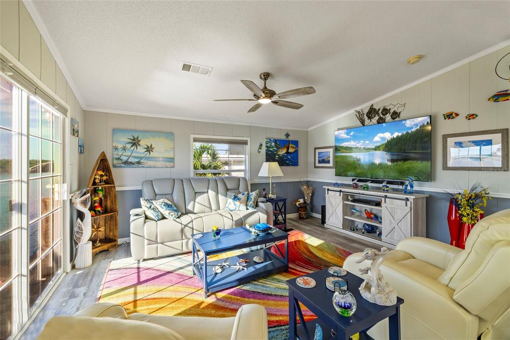 A living room features a colorful area rug, light-colored furniture, and a large wall-mounted television — 3413 BAYSIDE PARKWAY, PUNTA GORDA, FL