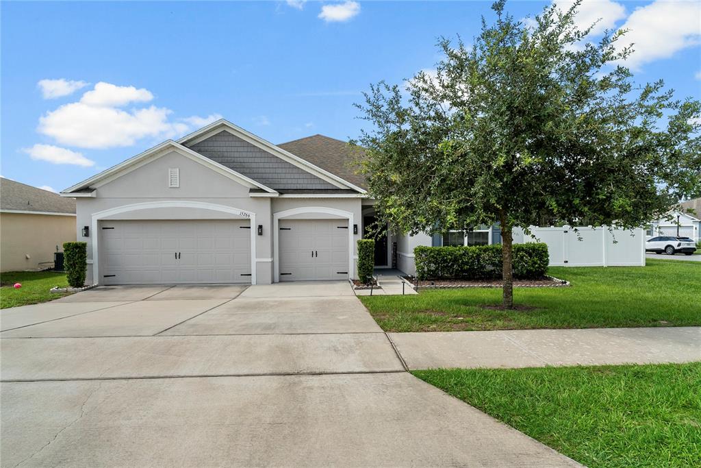 A single-story house with a three-car garage, a concrete driveway, and a large front tree — 15266 AQUARIUS WAY, MASCOTTE, FL