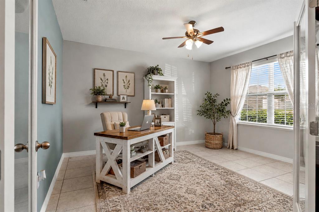 A home office features a wooden desk, a bookshelf, a ceiling fan, and a patterned rug — 15266 AQUARIUS WAY, MASCOTTE, FL