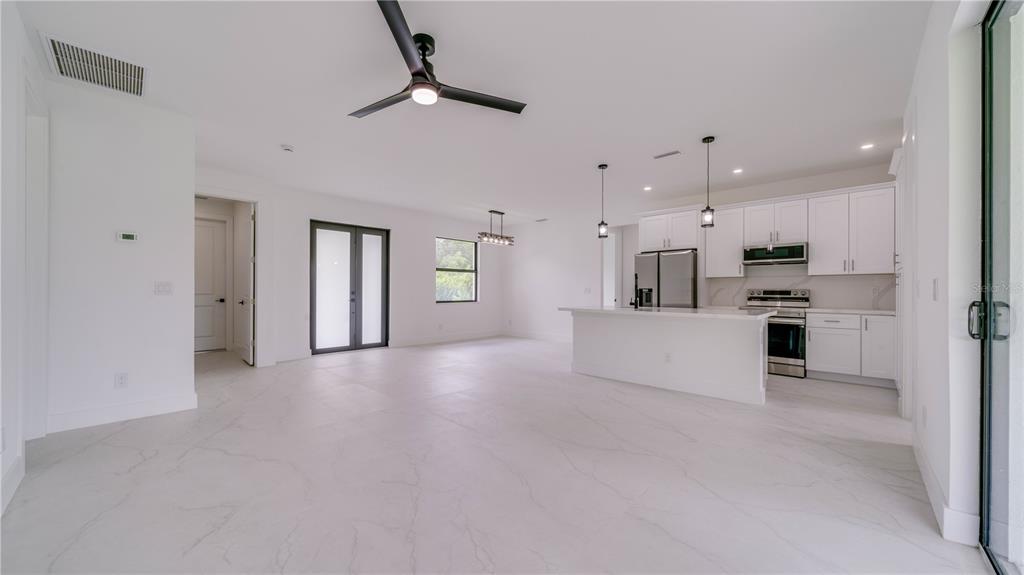 An open-concept kitchen and living area features white cabinetry, marble-look tile flooring, and recessed lighting — 2713 8TH STREET W, LEHIGH ACRES, FL