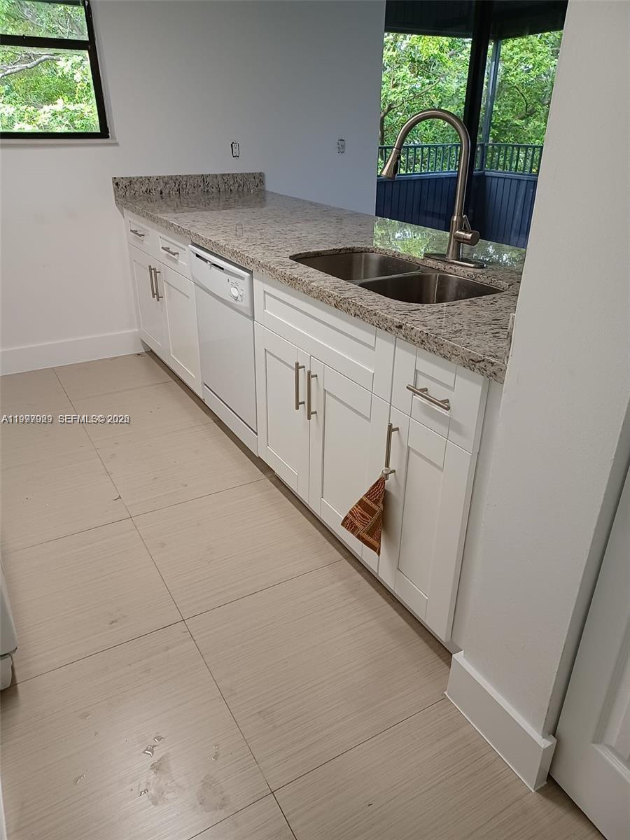 A kitchen features white cabinets, granite countertops, a stainless steel sink, and light-colored tile flooring — 16220 NW 2nd Ave # 411, Miami FL 33169, MIAMI, FL