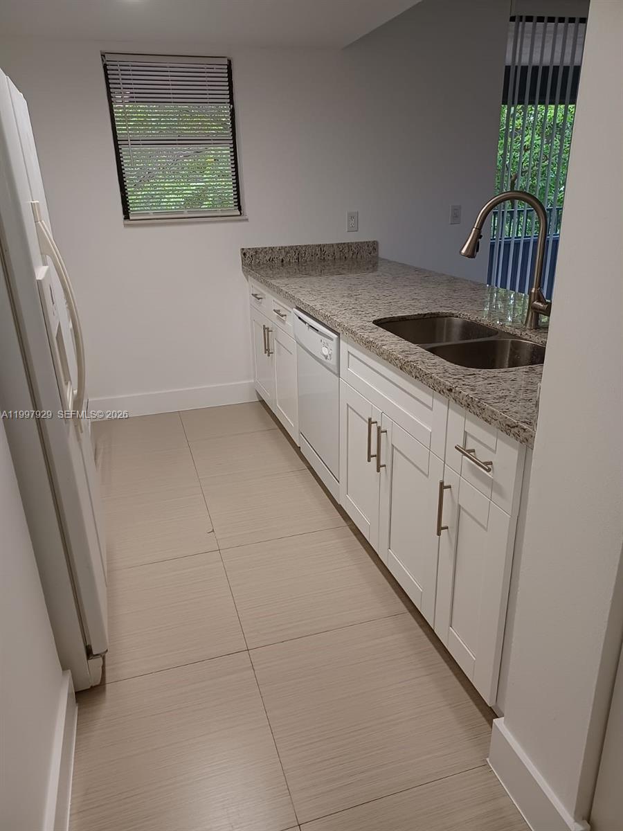 A kitchen features white cabinets, granite countertops, a stainless steel sink, and light tile flooring — 16220 NW 2nd Ave # 411, Miami FL 33169, MIAMI, FL