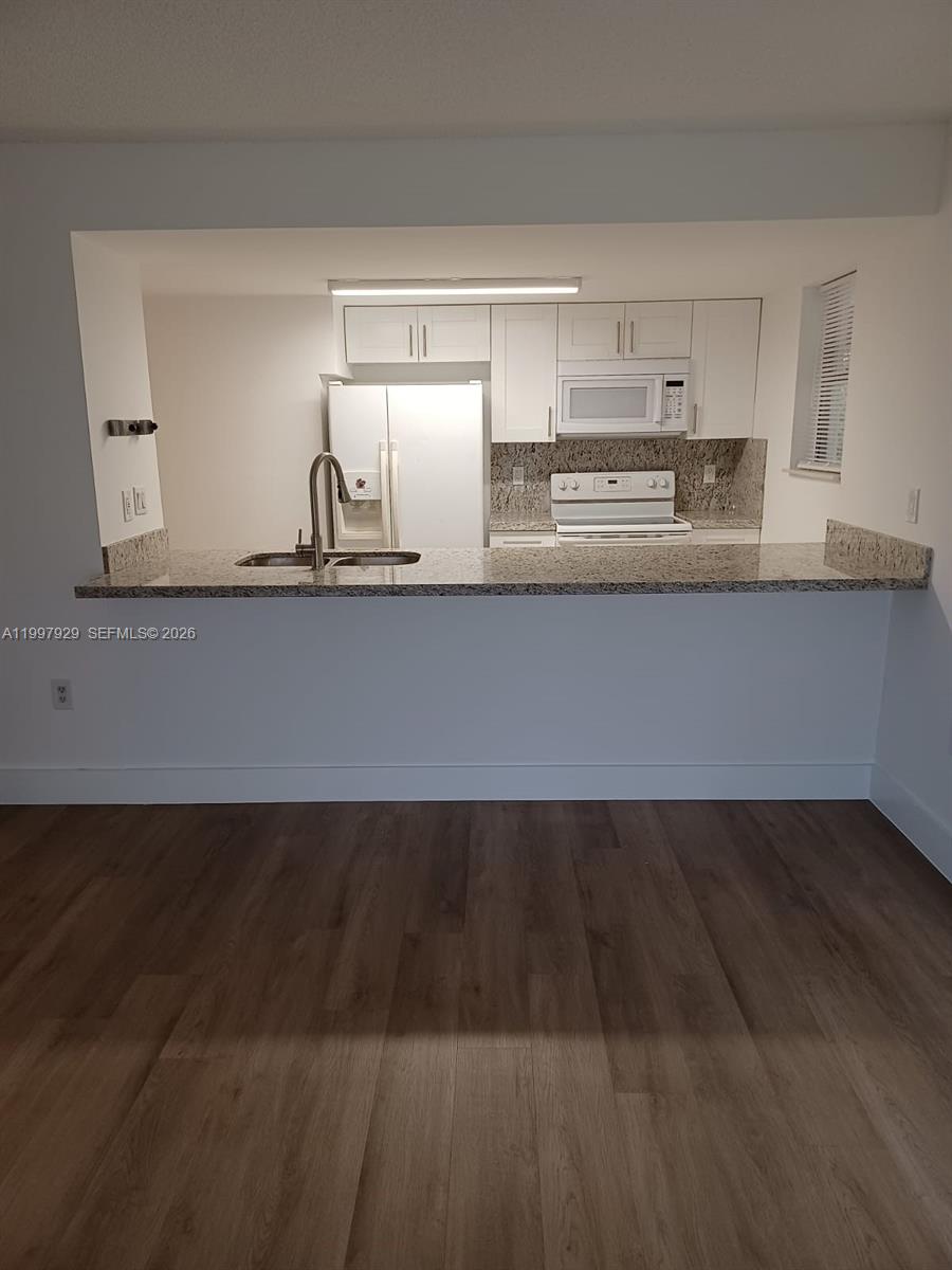 A kitchen with white cabinets, granite countertops, and stainless steel appliances overlooks a living area — 16220 NW 2nd Ave # 411, Miami FL 33169, MIAMI, FL