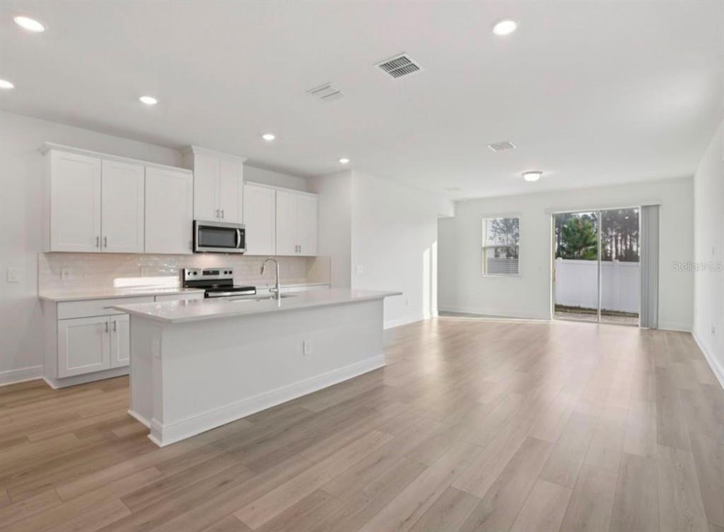 A modern kitchen with white cabinets and a center island opens into a spacious living area — 1769 ARCHER DRIVE, MINNEOLA, FL