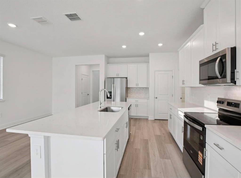 A modern kitchen features white cabinetry, a large center island, and light wood-look flooring — 1769 ARCHER DRIVE, MINNEOLA, FL