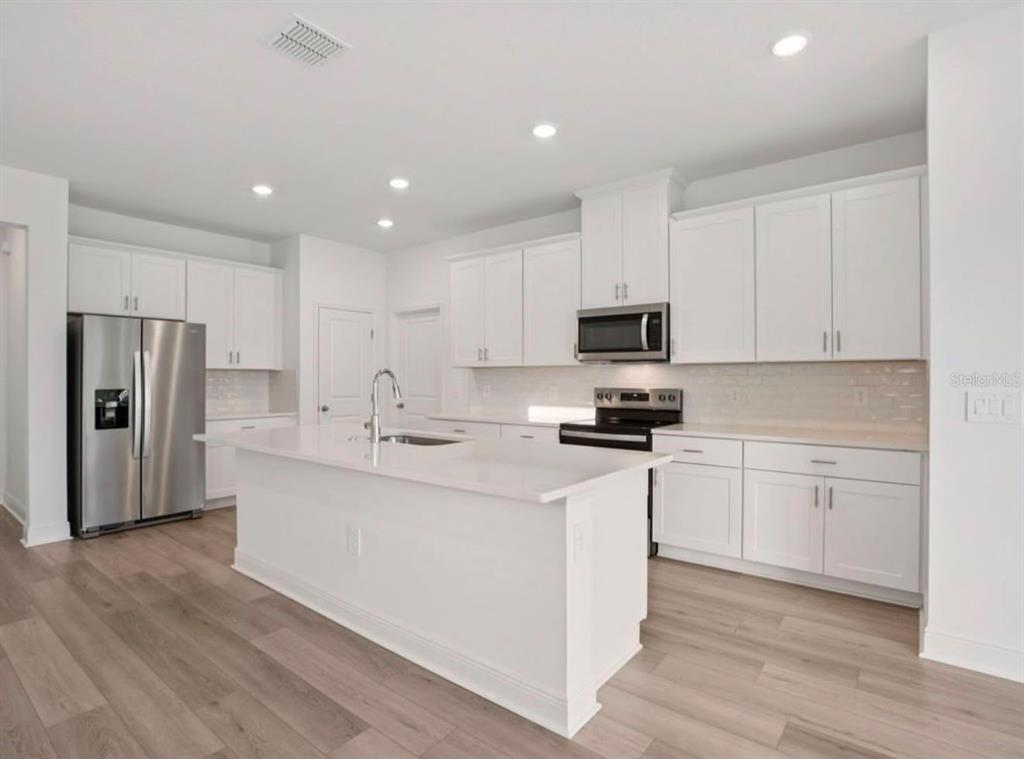 A modern kitchen features white cabinets, stainless steel appliances, a center island, and wood flooring — 1769 ARCHER DRIVE, MINNEOLA, FL