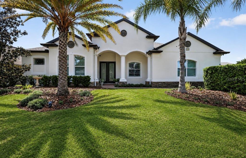 A single-story house with a white stucco facade, arched entryway, and two palm trees — 8237 BRIDGEPORT BAY CIRCLE, MOUNT DORA, FL