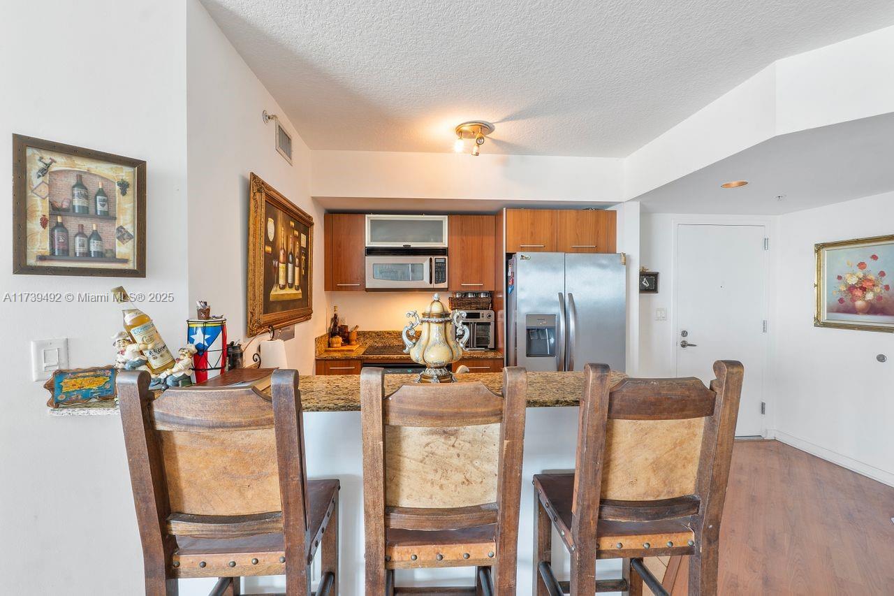 A kitchen features wooden cabinets, stainless steel appliances, granite countertops, and three rustic wooden chairs — 9055 SW 73rd Ct # 903, Miami FL 33156, MIAMI, FL