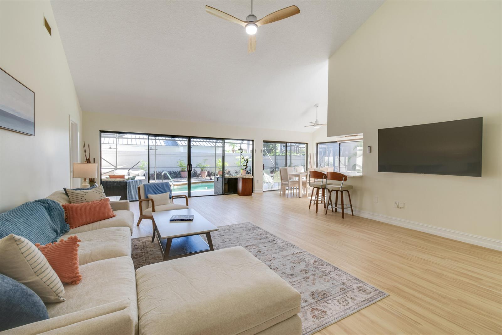 A bright living room features a sectional sofa, a wall-mounted television, and sliding glass doors — 137 Harbourside Circle, Jupiter FL 33477, JUPITER, FL