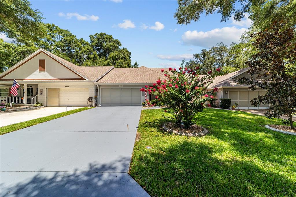 A wide, single-story house with a gray driveway, three garage doors, and a flowering tree — 8649 SW 92ND PLACE UNIT B, OCALA, FL