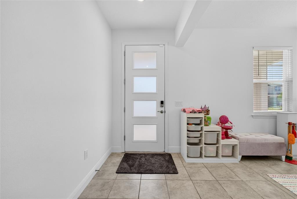 An entryway with tiled flooring, a white front door with glass panels, and toy storage — 2263 RAVEN RIDGE, CLERMONT, FL