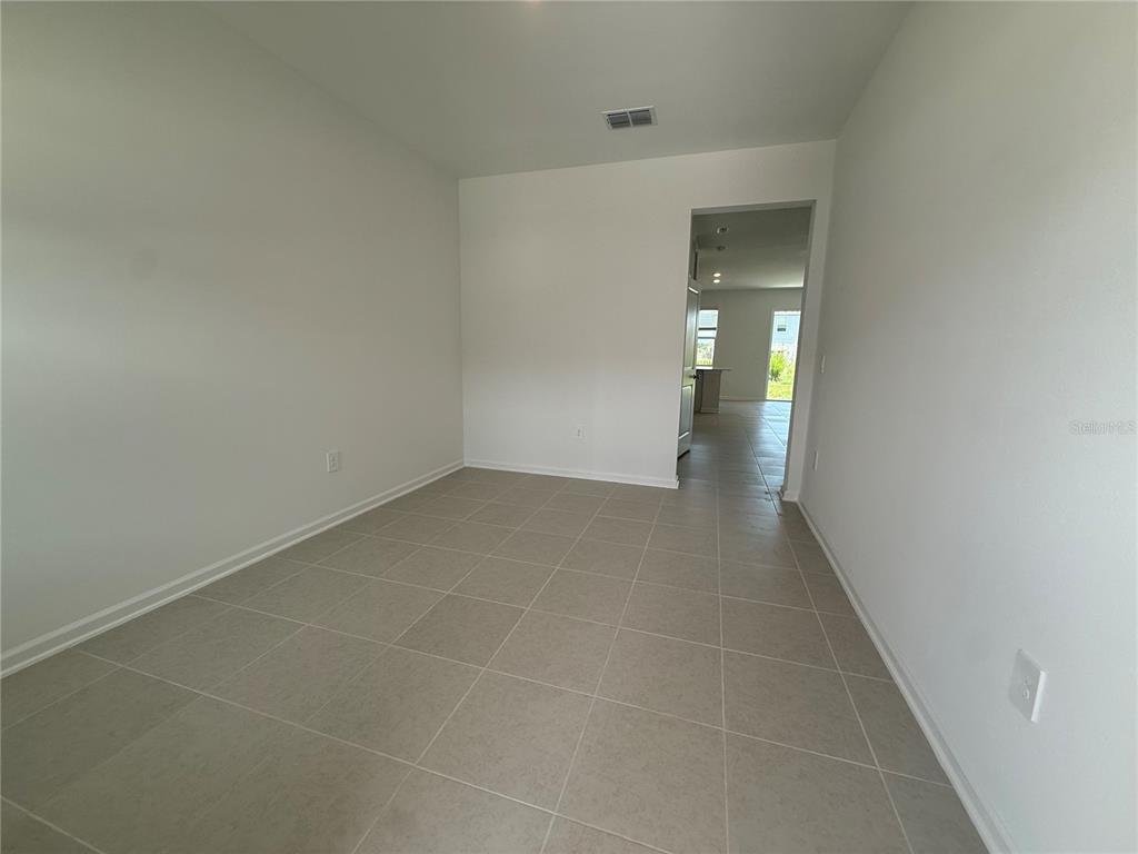 An empty room with light-colored walls and large square floor tiles leads to a hallway — 2567 SKYLINE LOOP, KISSIMMEE, FL