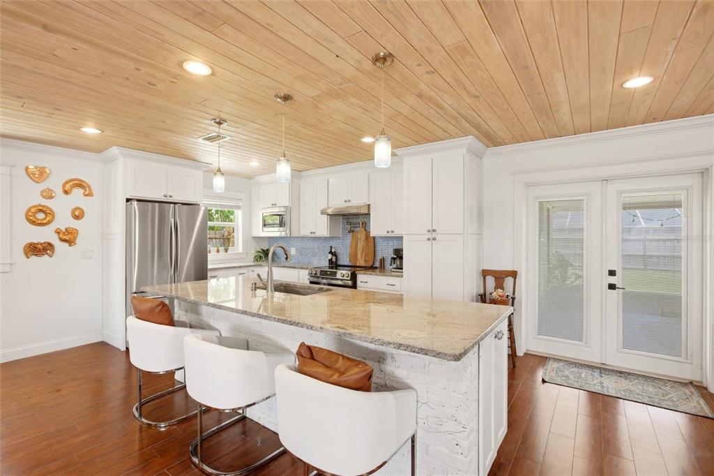 A kitchen features white cabinets, a granite island with bar stools, and a wood-plank ceiling — 706 18TH AVENUE DRIVE W, PALMETTO, FL