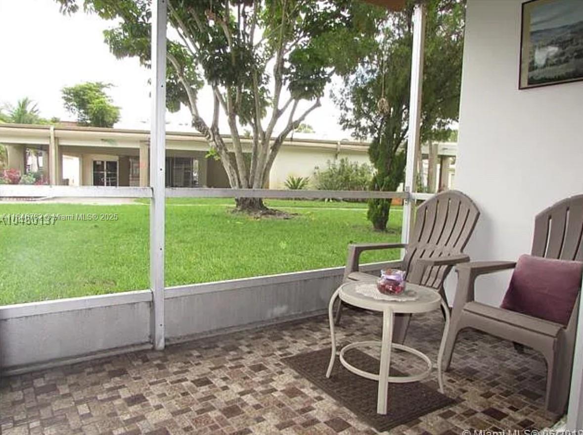 A screened-in patio features tiled flooring, two chairs, a small table, and a grassy view — 1530 NE 191st St # 145, Miami FL 33179, MIAMI, FL