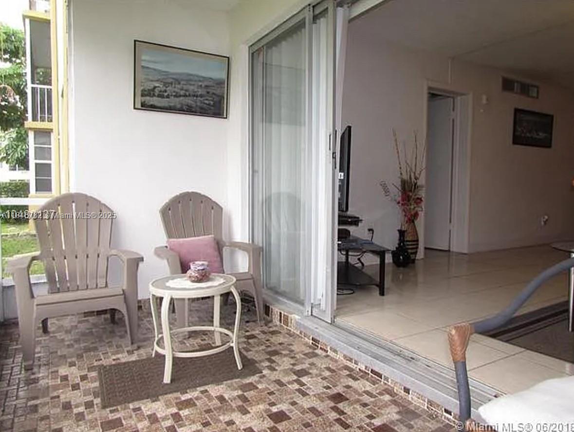 A covered balcony with tiled flooring features two chairs and a small table — 1530 NE 191st St # 145, Miami FL 33179, MIAMI, FL
