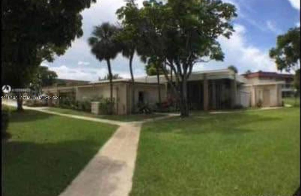 A low-rise residential building is surrounded by a grassy lawn and mature trees — 1530 NE 191st St # 145, Miami FL 33179, MIAMI, FL