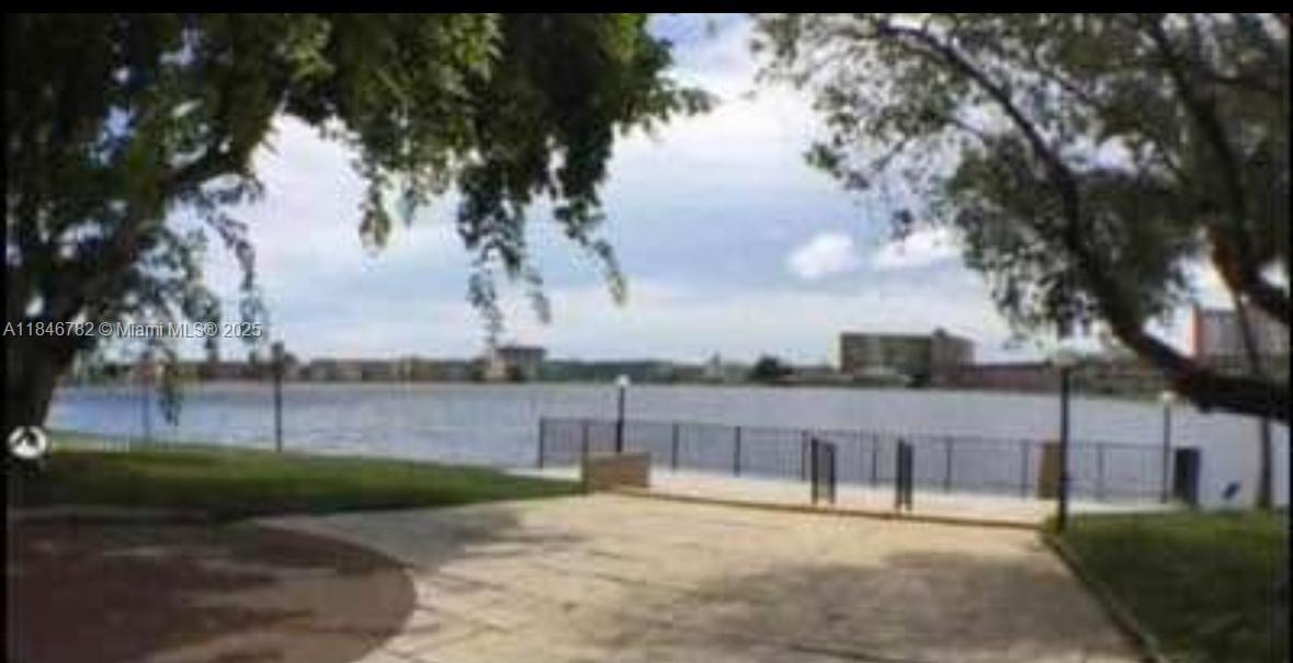A paved walkway leads to a waterfront area with a metal railing and trees — 1530 NE 191st St # 145, Miami FL 33179, MIAMI, FL