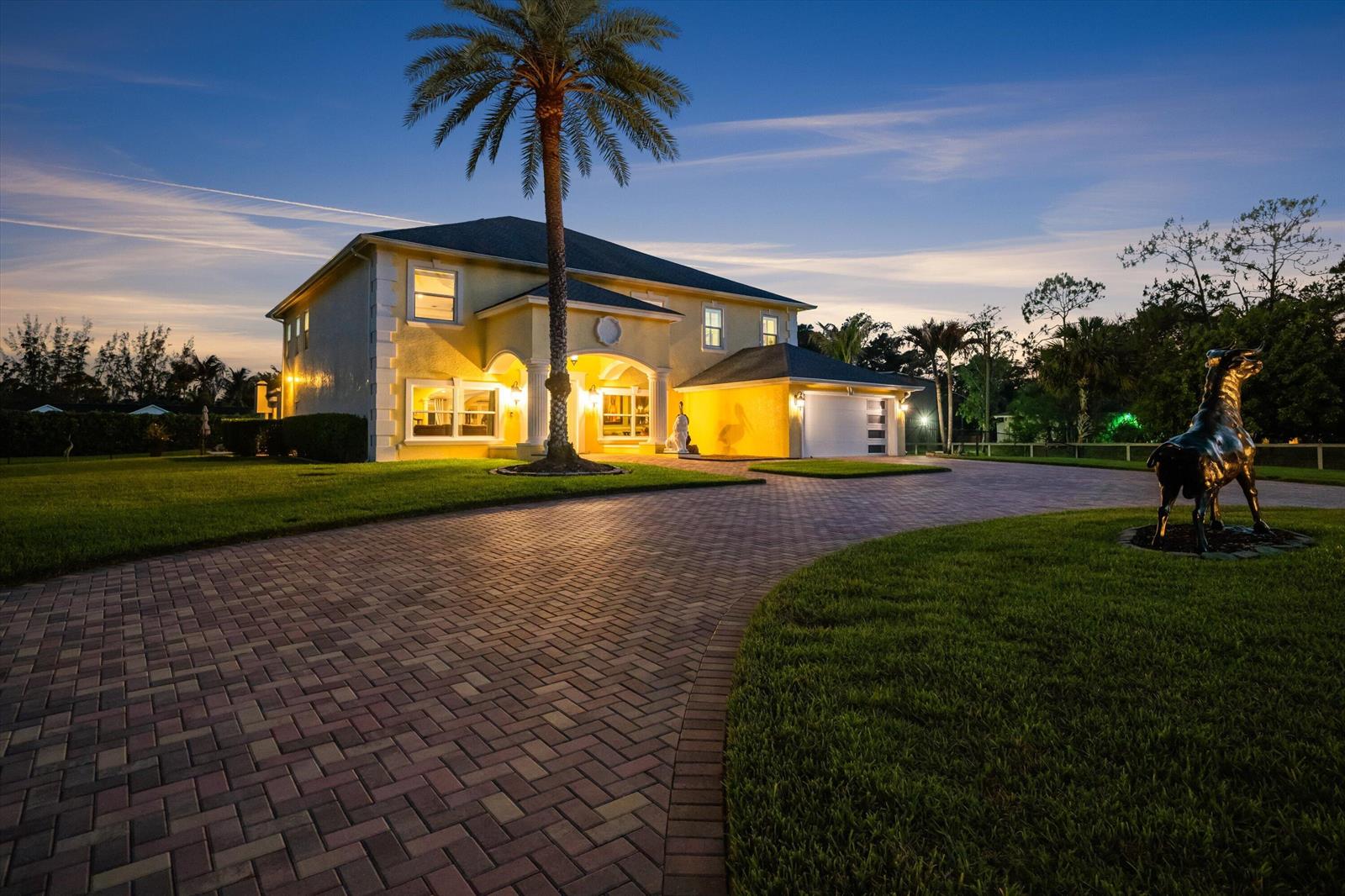 A two-story yellow house with a brick driveway, a palm tree, and a bull statue — 17948 N 33rd Rd Road N, FL 33470, FL