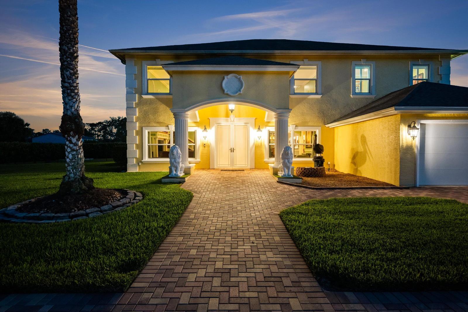 A two-story yellow house with a brick walkway, white columns, and two lion statues — 17948 N 33rd Rd Road N, FL 33470, FL
