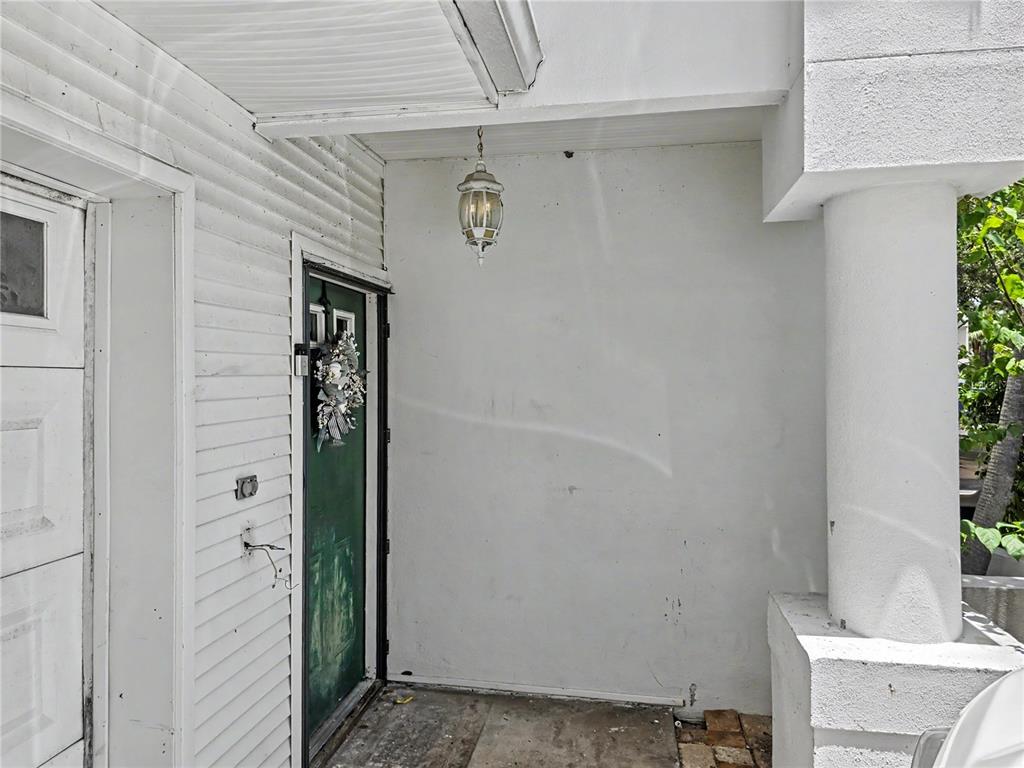 A white covered porch features a green front door, a hanging lantern, and a column — 9870 INDIAN KEY TRAIL UNIT 64, SEMINOLE, FL
