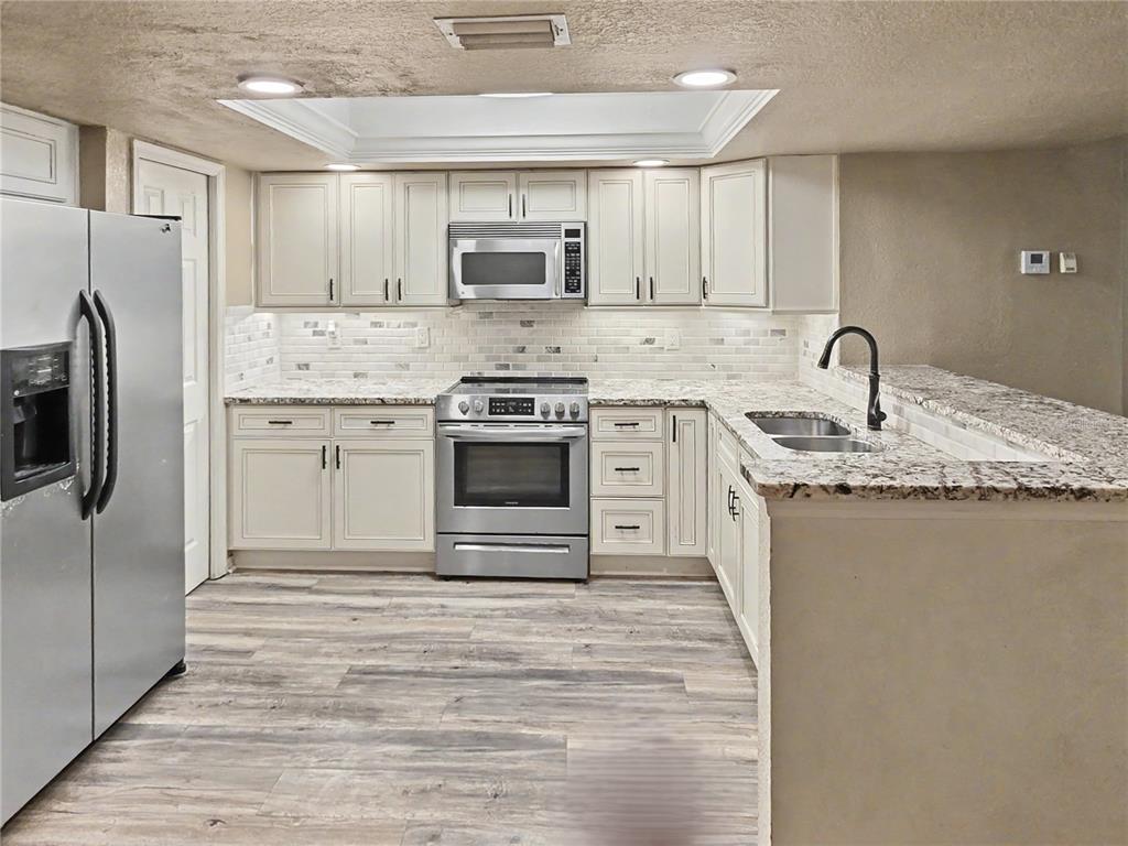 A kitchen features stainless steel appliances, light-colored cabinets, granite countertops, and wood-look flooring — 9870 INDIAN KEY TRAIL UNIT 64, SEMINOLE, FL