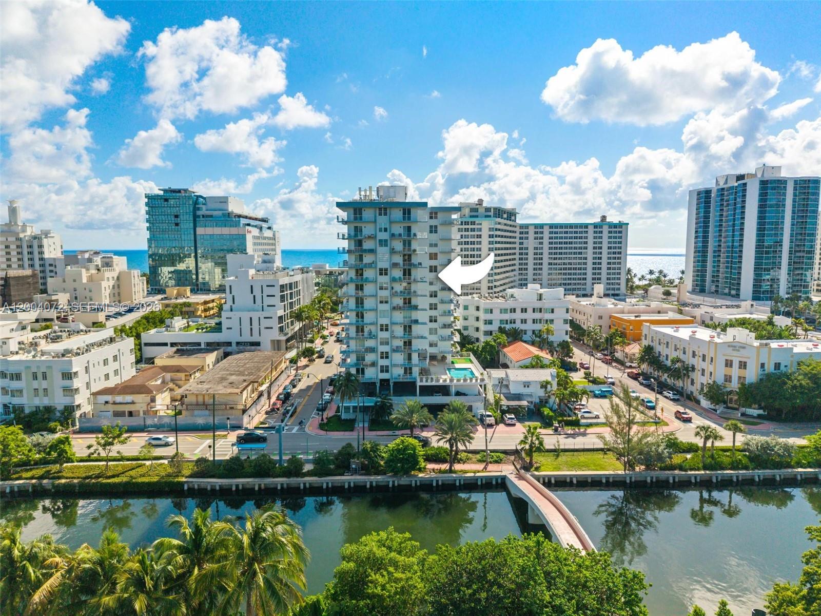 An aerial view shows a tall residential building with a white arrow pointing toward it — 2829 Indian Creek Dr # 1002, Miami Beach FL 33140, MIAMI BEACH, FL
