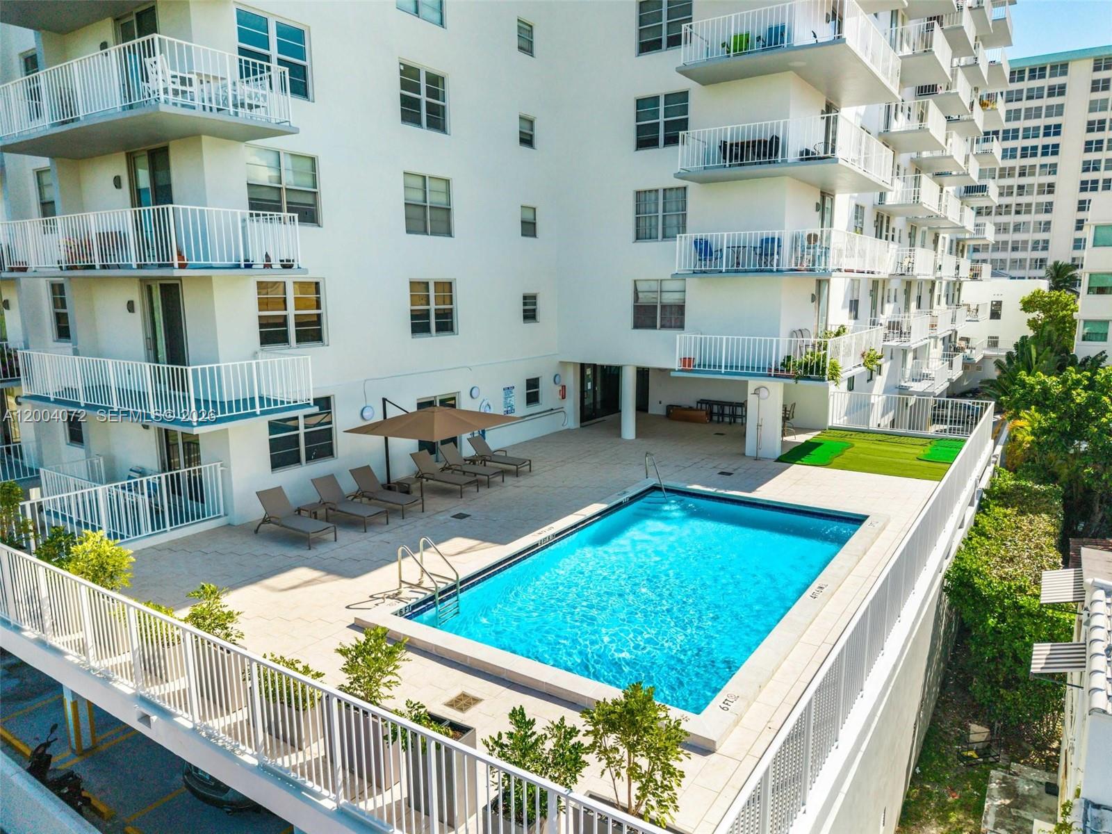 An elevated outdoor swimming pool area with lounge chairs and a patio next to apartments — 2829 Indian Creek Dr # 1002, Miami Beach FL 33140, MIAMI BEACH, FL