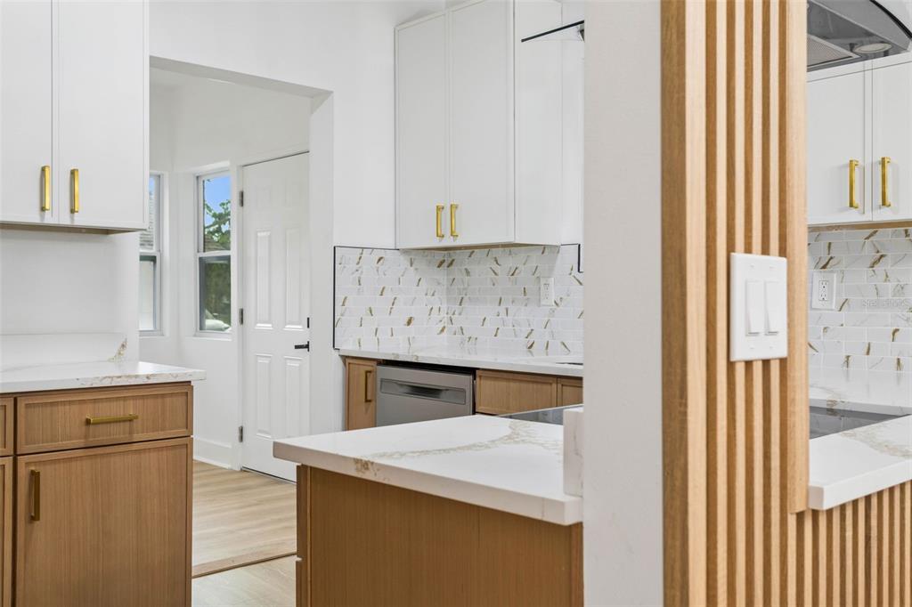 A kitchen features white upper cabinets, wood lower cabinets, gold hardware, and marble-patterned tile backsplashes — 4660 7TH AVENUE N, ST PETERSBURG, FL