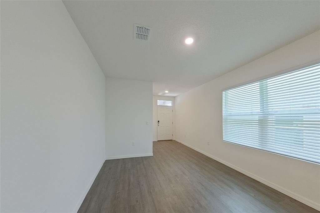 An empty room with gray wood-look flooring, white walls, and a window with blinds — 31962 KATELIN CIRCLE, LEESBURG, FL