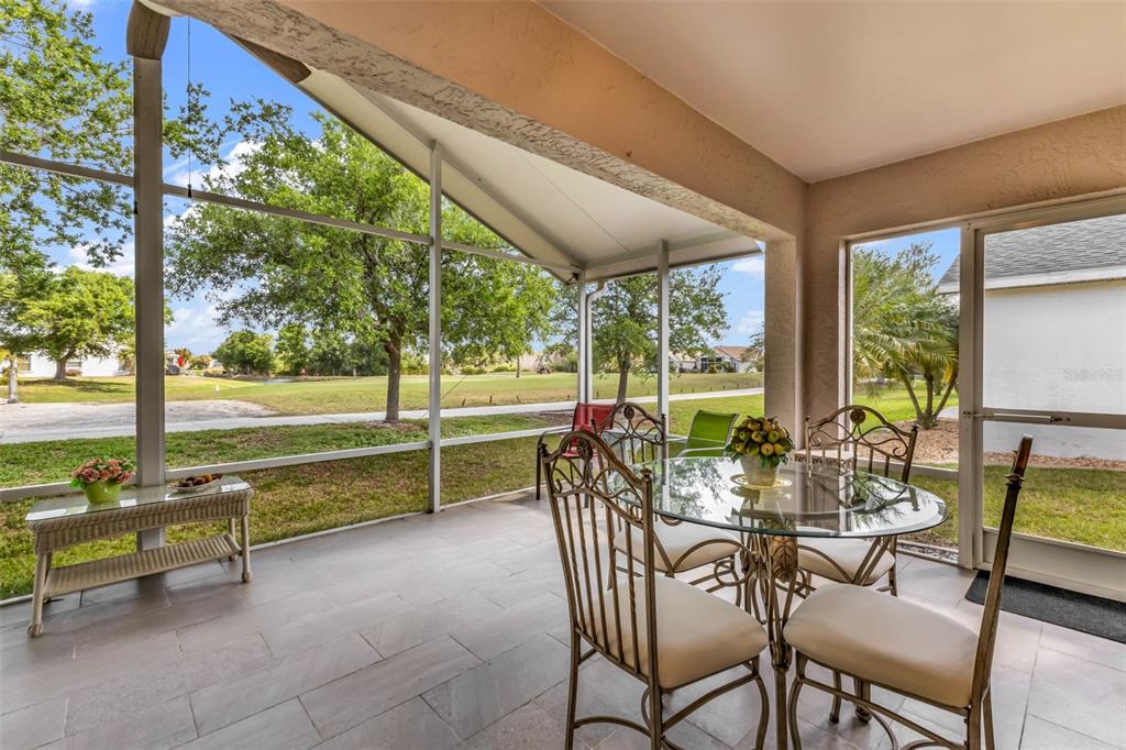 A screened-in patio features tile flooring, a glass dining set, and views of a golf course — 1869 BIRMINGHAM BOULEVARD, PUNTA GORDA, FL