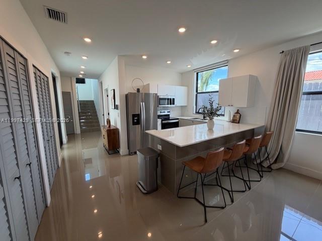 A modern kitchen features white cabinetry, a quartz island with bar seating, and tile flooring — 3645 SW 3 st, Miami FL 33135, MIAMI, FL