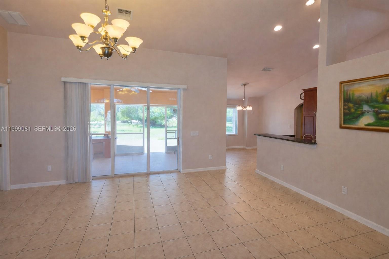 A tiled living area features a chandelier, sliding glass doors, and an adjacent kitchen — 825 Costa Pl, Lehigh Acres FL 33972, LEHIGH ACRES, FL