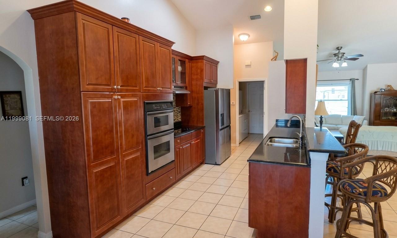 A kitchen features cherry wood cabinets, stainless steel appliances, and a black granite breakfast bar — 825 Costa Pl, Lehigh Acres FL 33972, LEHIGH ACRES, FL
