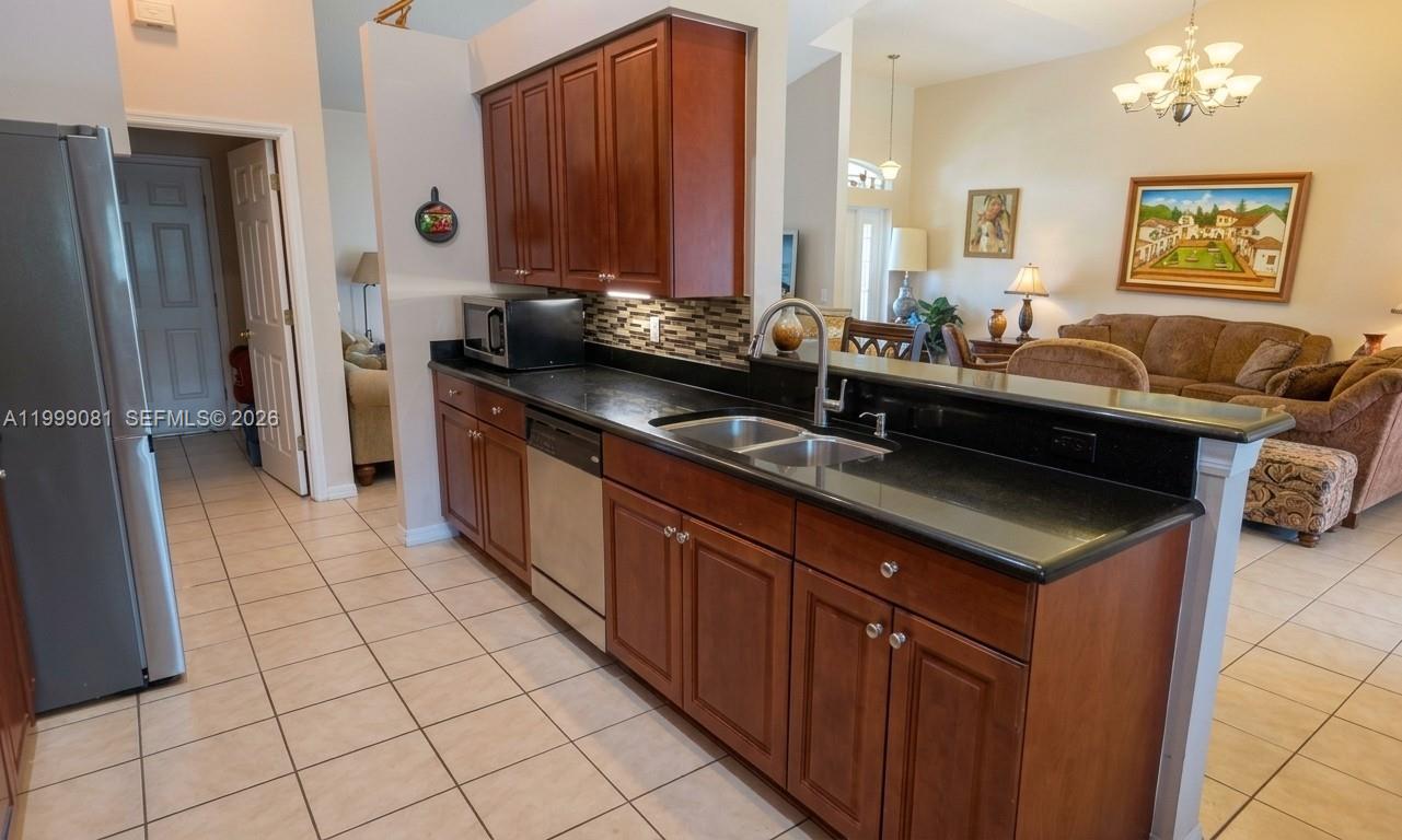 A kitchen with dark wood cabinets, black countertops, and stainless steel appliances overlooks a living area — 825 Costa Pl, Lehigh Acres FL 33972, LEHIGH ACRES, FL