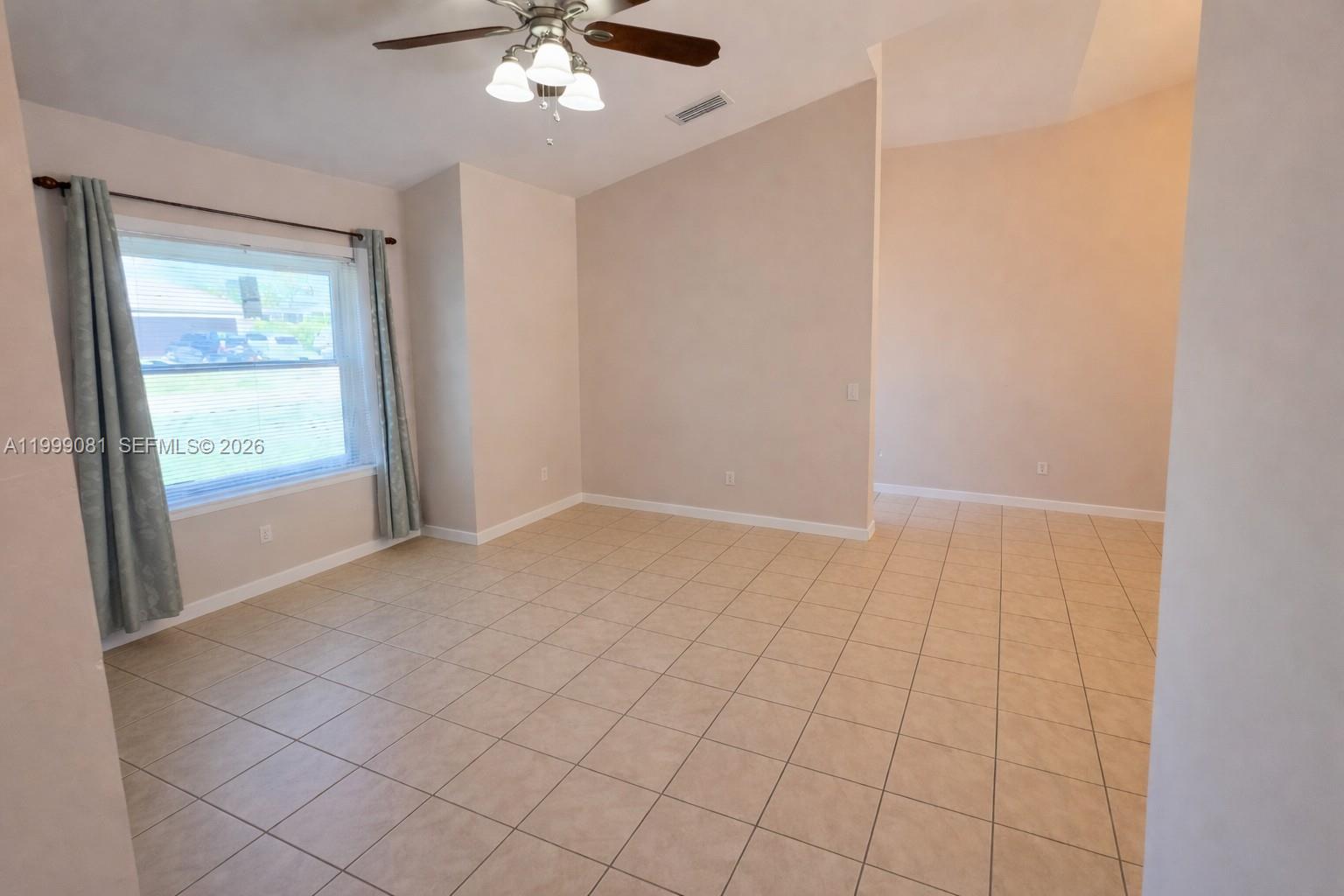 An empty room features beige tile flooring, a ceiling fan, and a large window — 825 Costa Pl, Lehigh Acres FL 33972, LEHIGH ACRES, FL